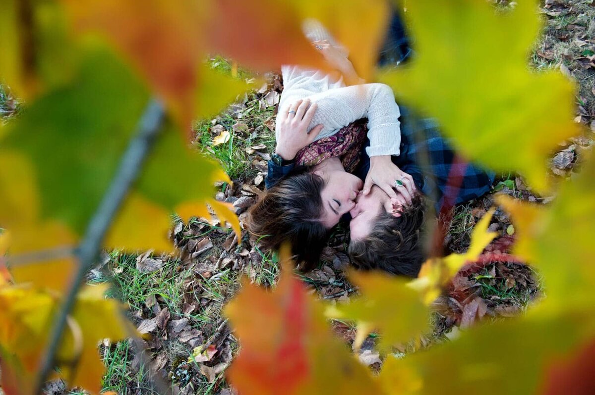 a man and woman lay on the ground underneath a tree full of fall colored leaves