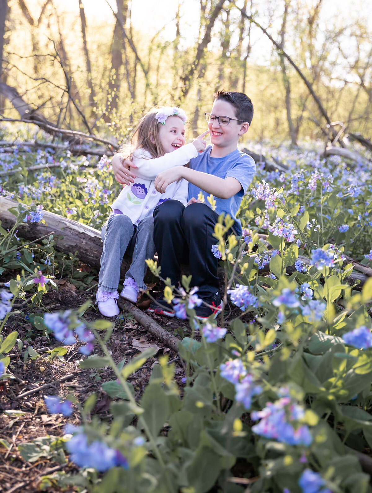 A brother and sister poke eachother playfully and laugh while the photographer takes their picture in Harford County, Maryland during a bluebells photoshoot.