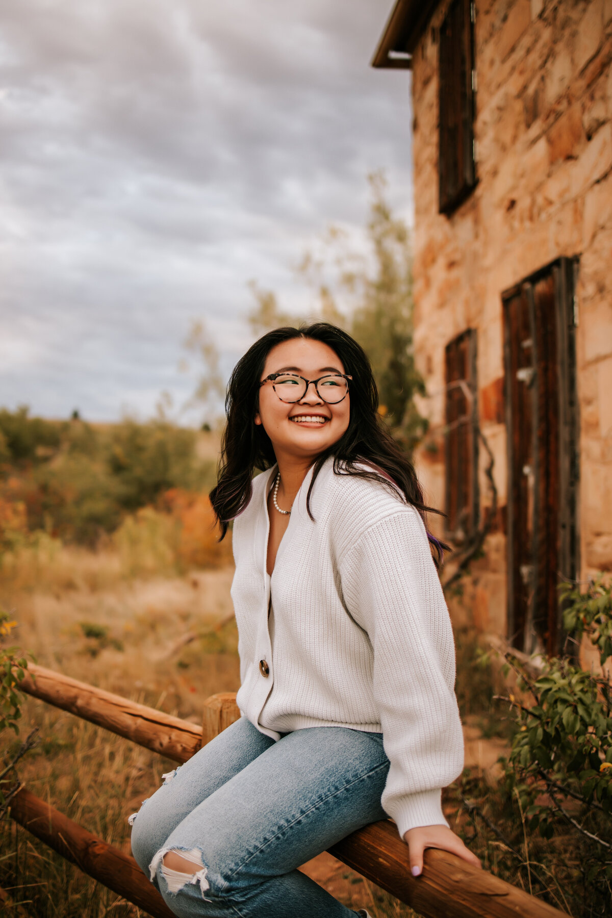 girl sits on fence wearing  a white sweater in boulder colorado for senior session