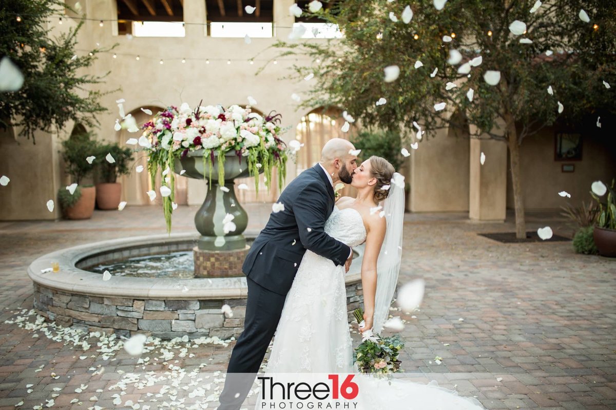 Groom dips his Bride as he kisses her in front of the fountain