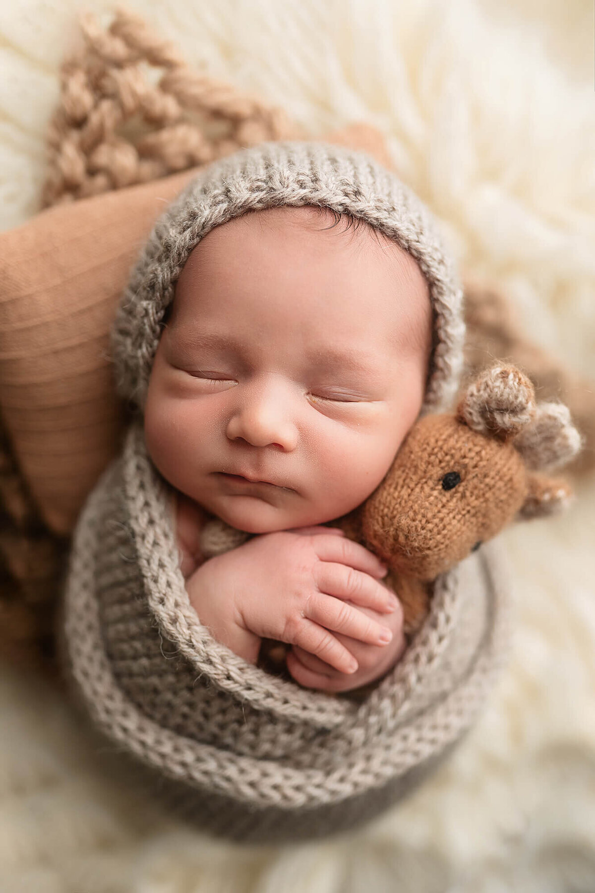 Newborn boy wrapped in a knitted wrap holding a giraffe.