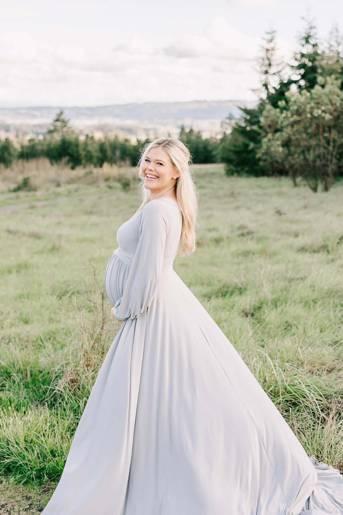 portland woman holding belly and smiling in field for maternity session
