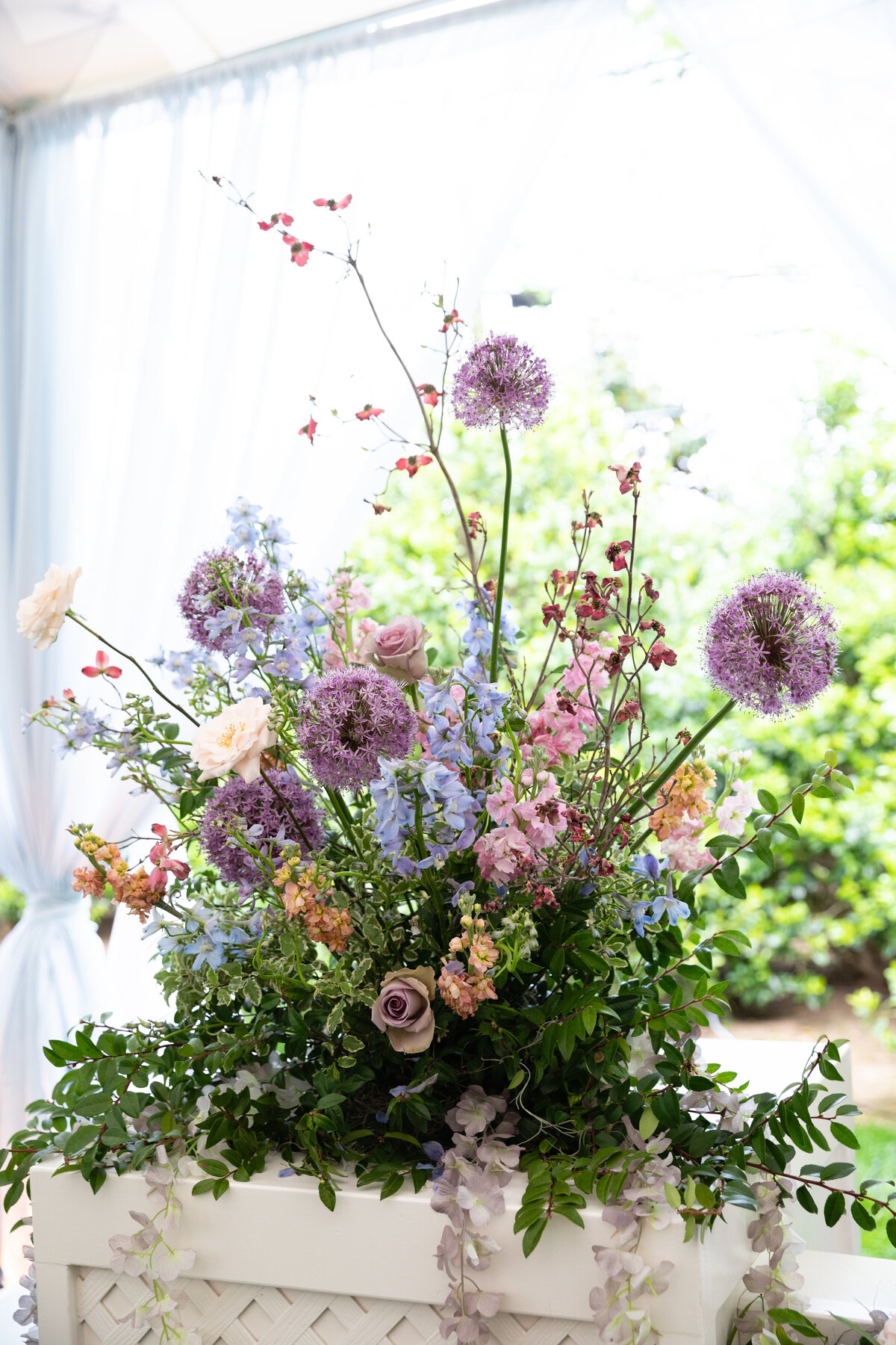 Growing, fresh floral installations with blush garden roses, lavender delphinium, wisteria, globe allium, and vines and greenery for a tented Bridgerton inspired engagement party at a private home in Nashville, TN. Flower by Tennessee based wedding f