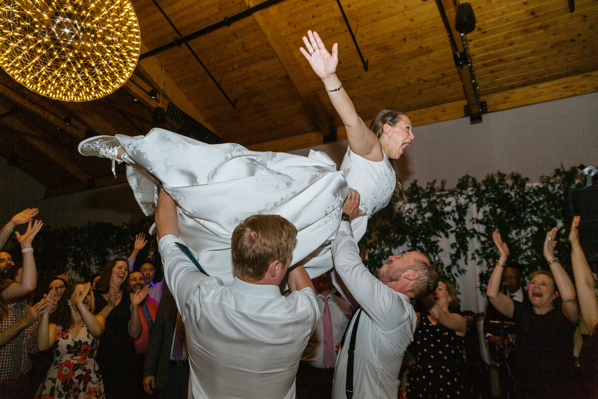 A bride being lifted up like she is flying by wedding guests.