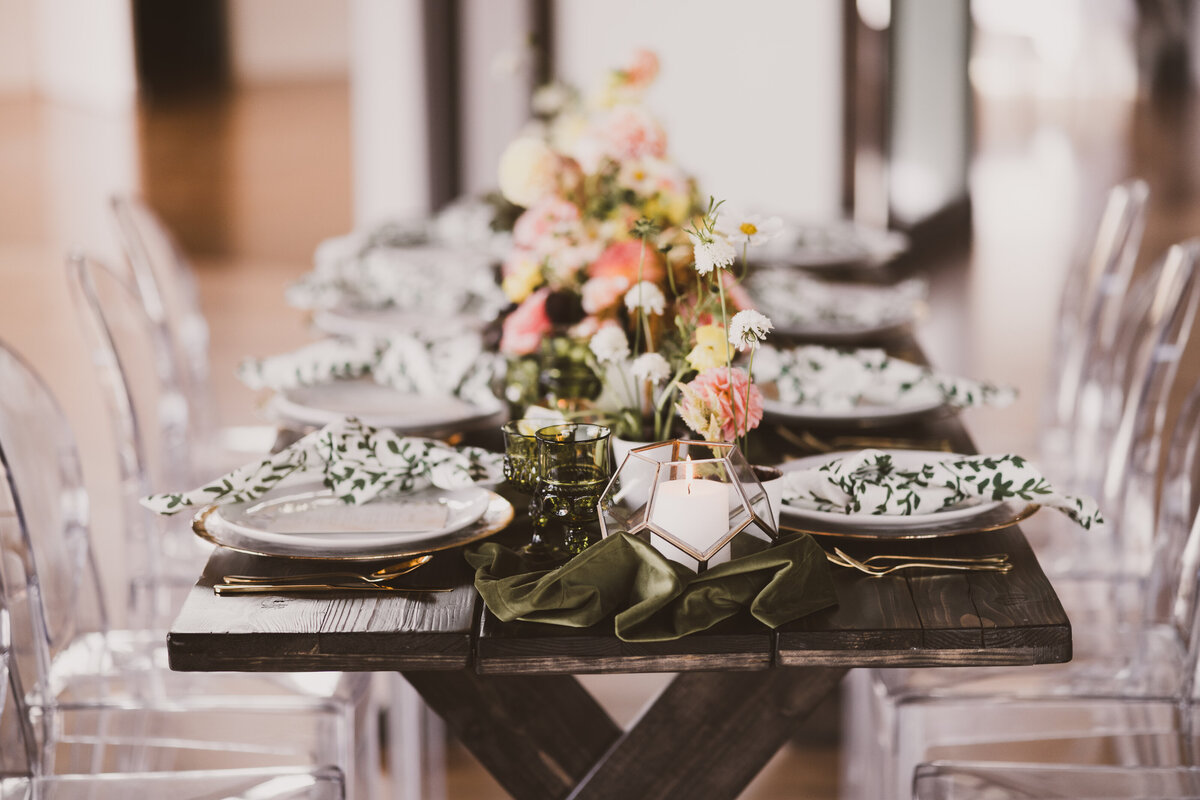 Romantic wedding reception tablescape with green runner, ghost chairs and farm table