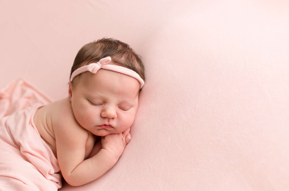 Baby girl on pink backdrop with tiny pink bow