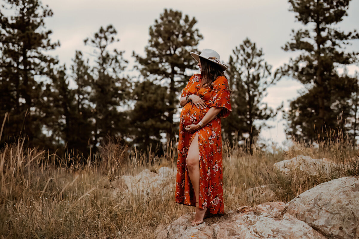 pregnant mom holds belly while wearing a floarl orange maternity dress