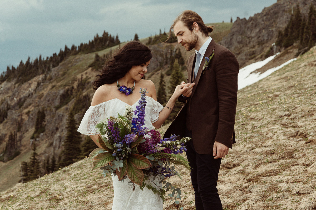 bride and groom hold hands at Olympic National Park, bride holds a purple bouquet and groom wears brown suit