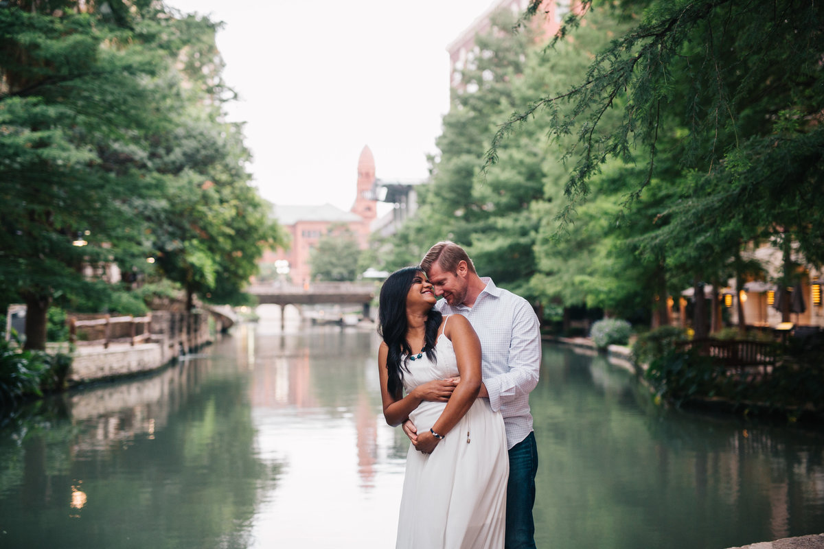Pregnant couple holding each other in front of the San Antonio River Walk for their maternity photography session.