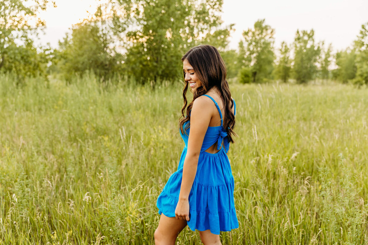 stunning young woman in a short blue dress looking down at her feet during her Green Bay senior photography session