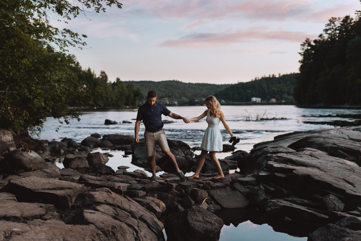 man holding his bride's hand as they walk across the rocks by the water