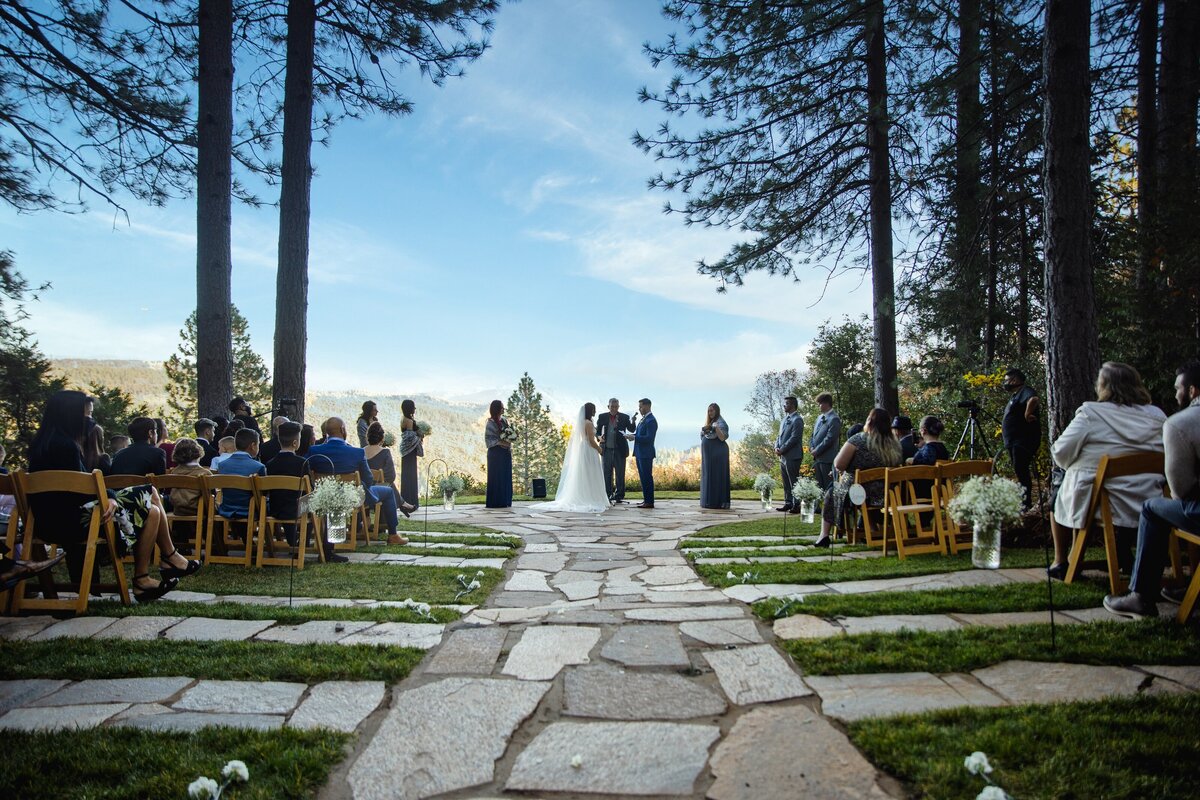 Wedding ceremony photo captured by philippe studio pro, at forest house lodge near sacramento where guests look on to couple giving their vows with forest mountains in the background.