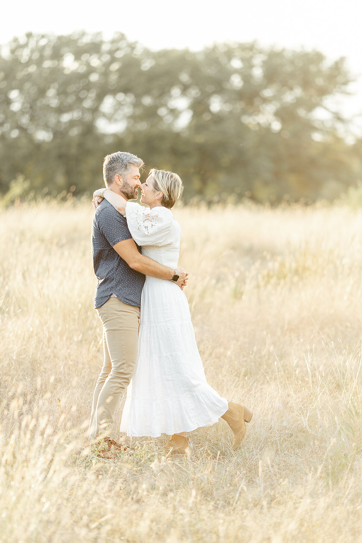 Photo of a mom and dad embracing each other in the middle of a grassy field at a local Fort Worth park for their family photos.