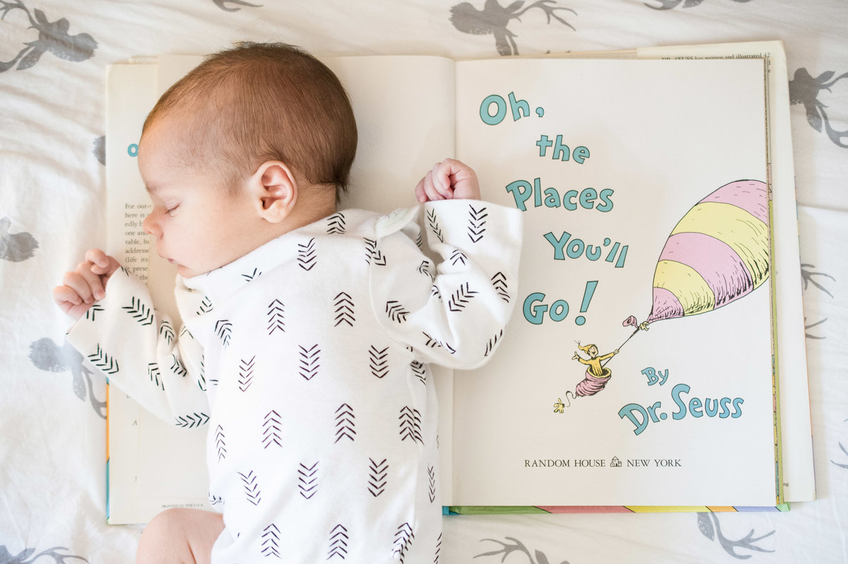 A newborn baby sleeps next to a Dr. Seuss book.