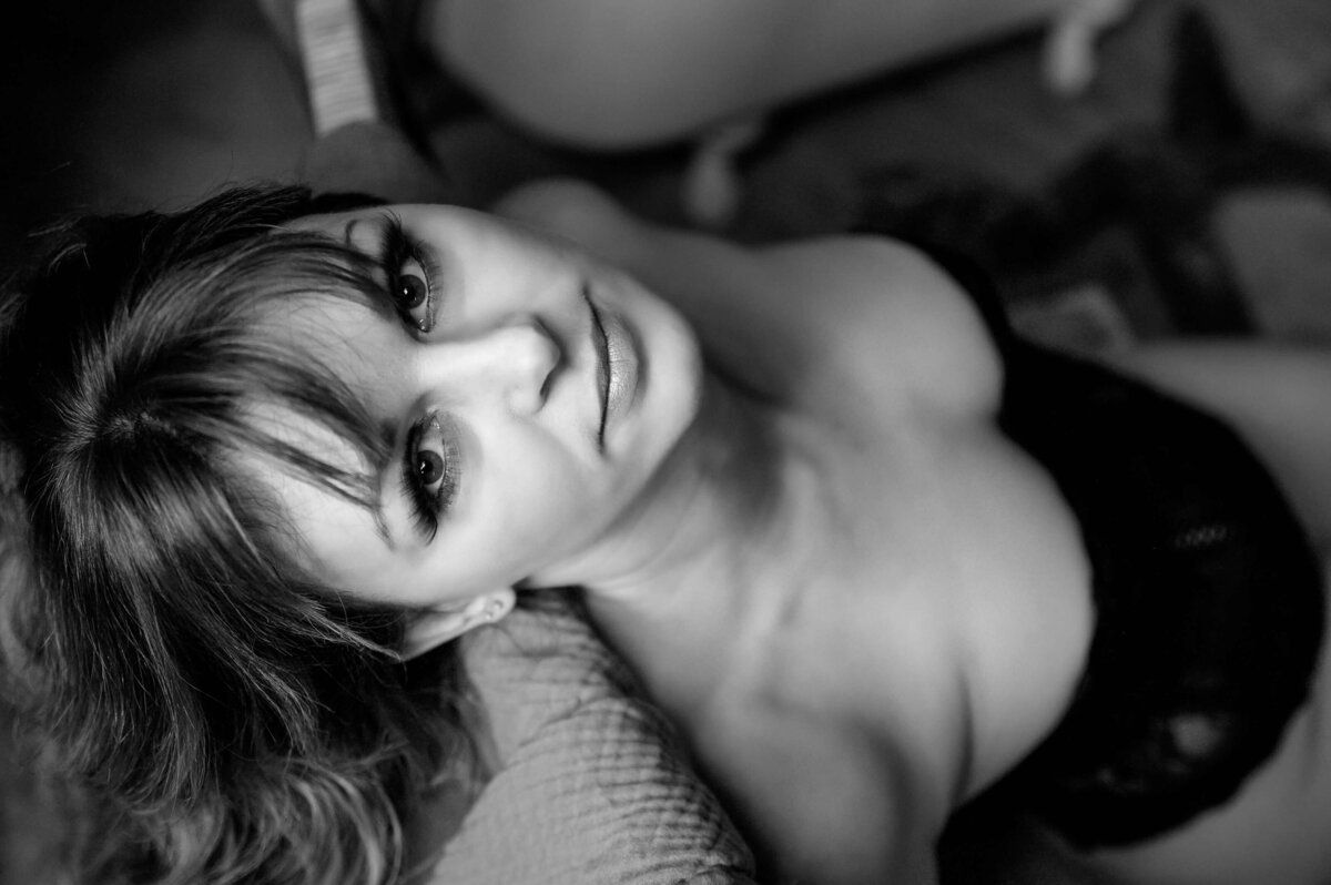 black and white photo of a woman in a black bodice with her head over a chair looking up at the camera for her Mississauga boudoir photography session