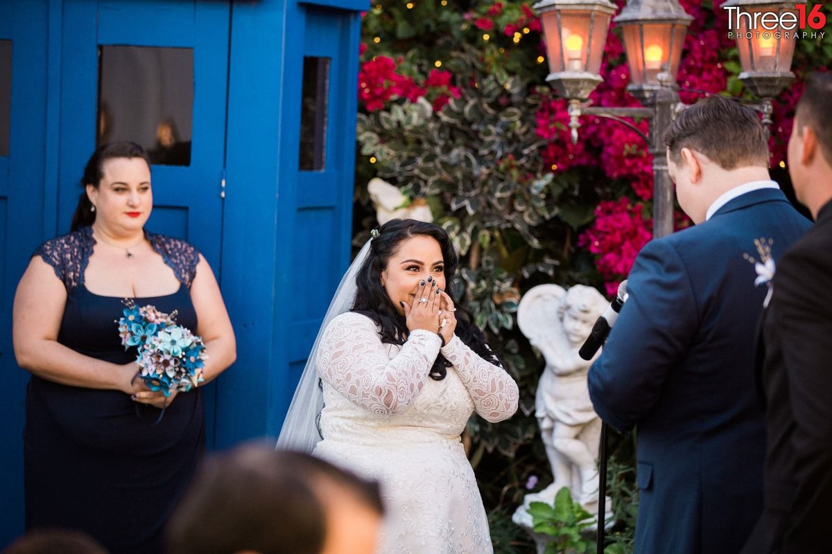 Bride covers her mouth  and smiles as her Groom reads his vows to her