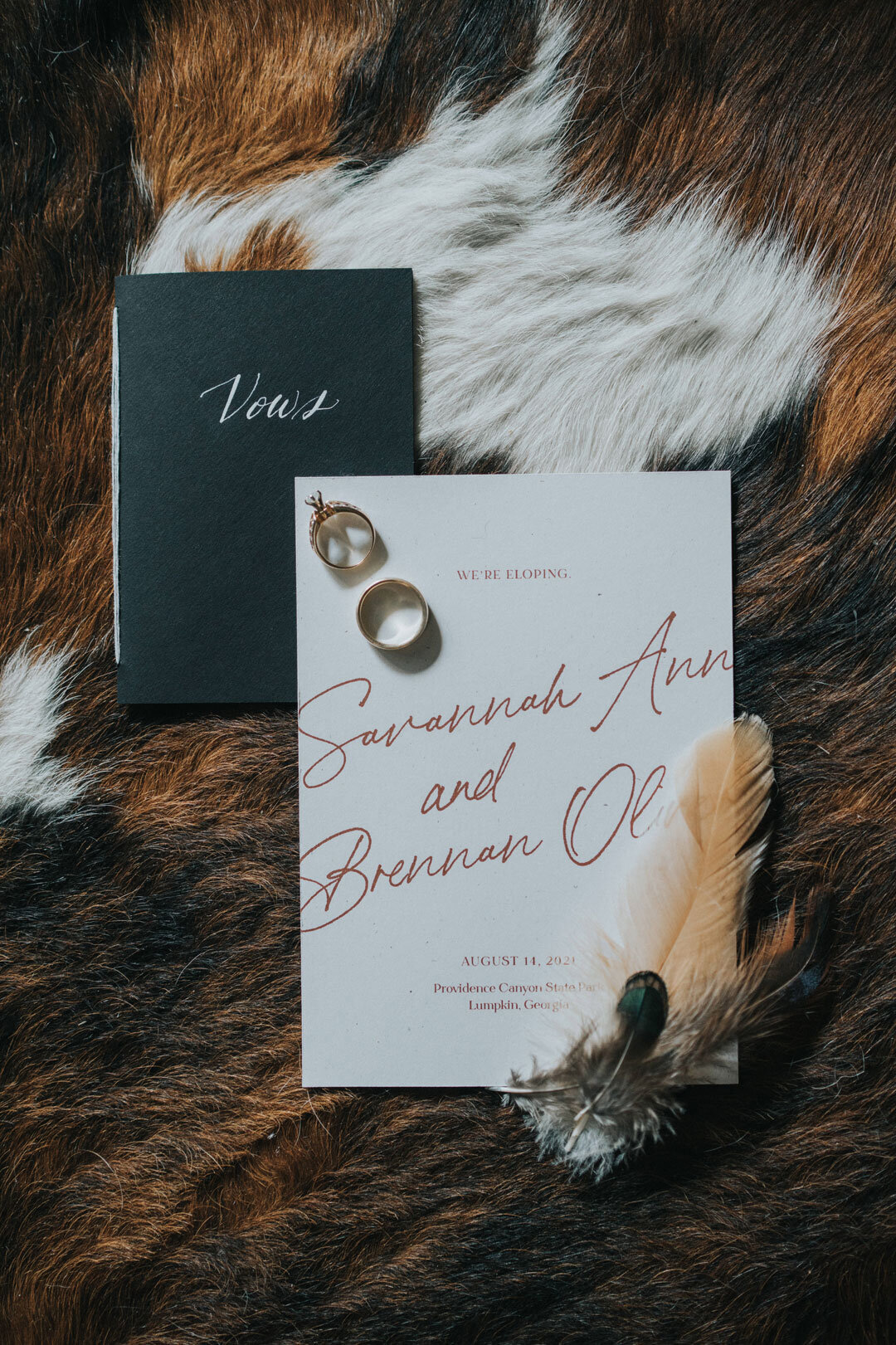 White wedding invitation with red script next to a feather and black vow book