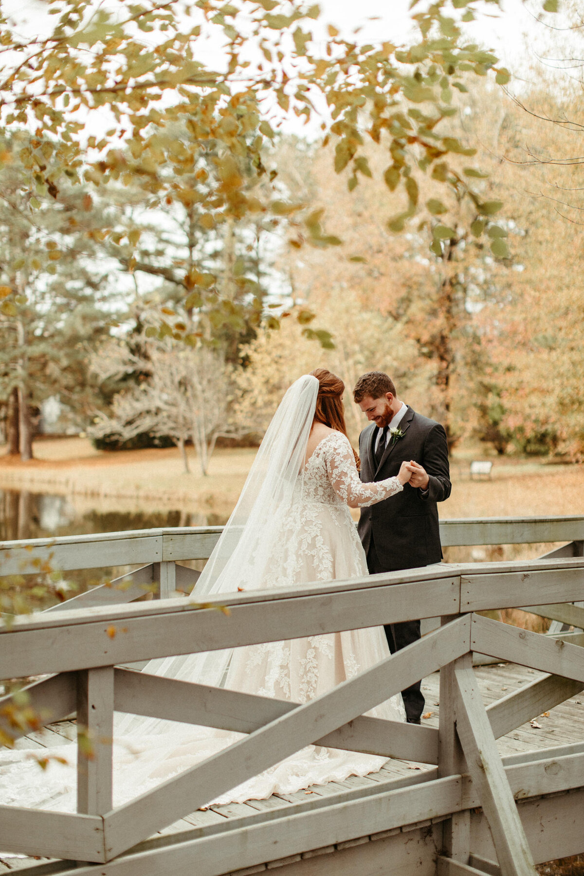 Groom excited to see his bride on a bridge over a pond with tree branches hanging over them on a fall ay