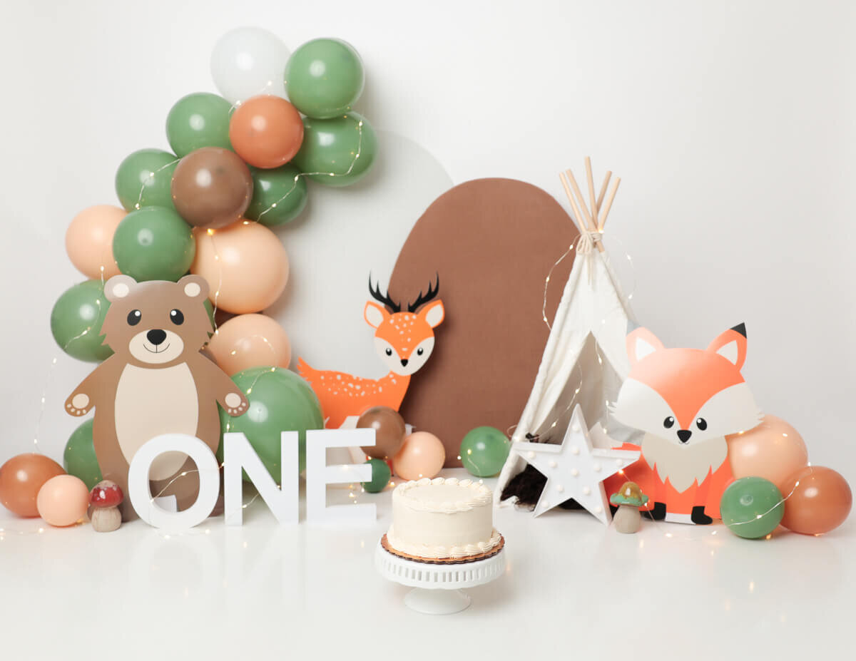 A whimsical woodland-themed setup, featuring a rustic cake adorned with forest animals, vibrant greenery, and playful props, capturing the essence of a cake smash photography session in Rochester, NY.