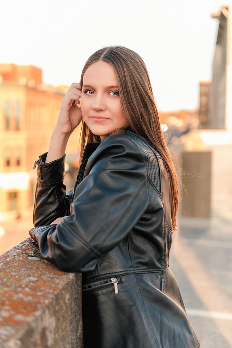 High school senior girl leaning on wall on roof of parking garage at sunset