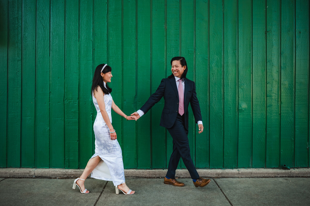 Chinese bride and groom walk in front of green wall in Chinatown