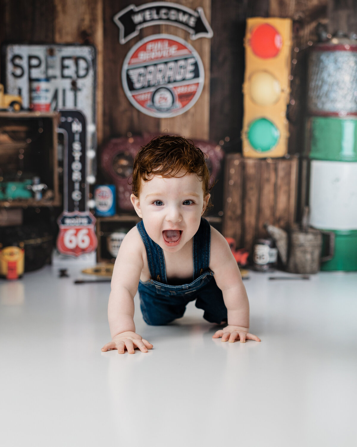 Smiling baby boy sitting on the floor in front of a rustic garage set, celebrating his first birthday in overalls.
Photograph by Yucaipa cake smash photographer Kaitlyn Dawn Photography.