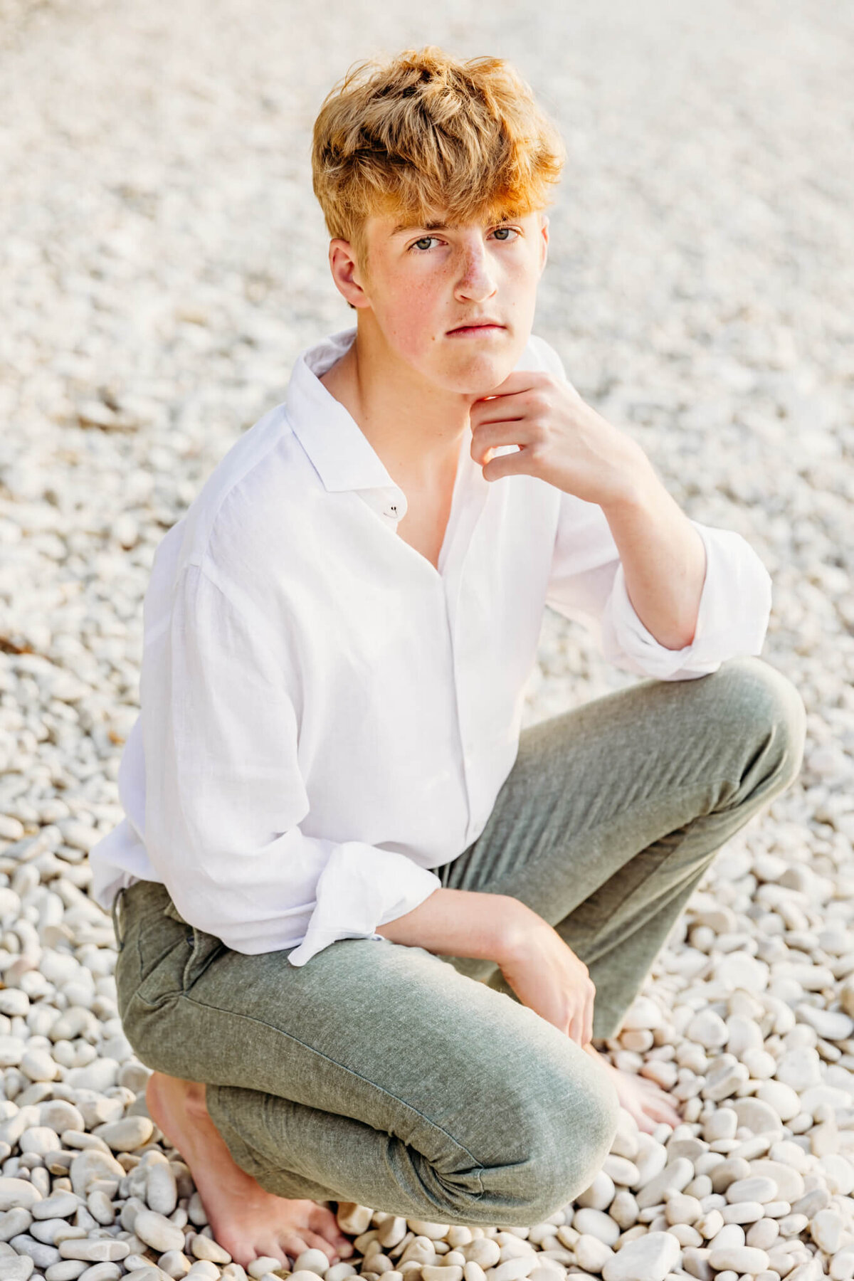 senior boy squatting and resting chin on hand for senior photos in Green Bay