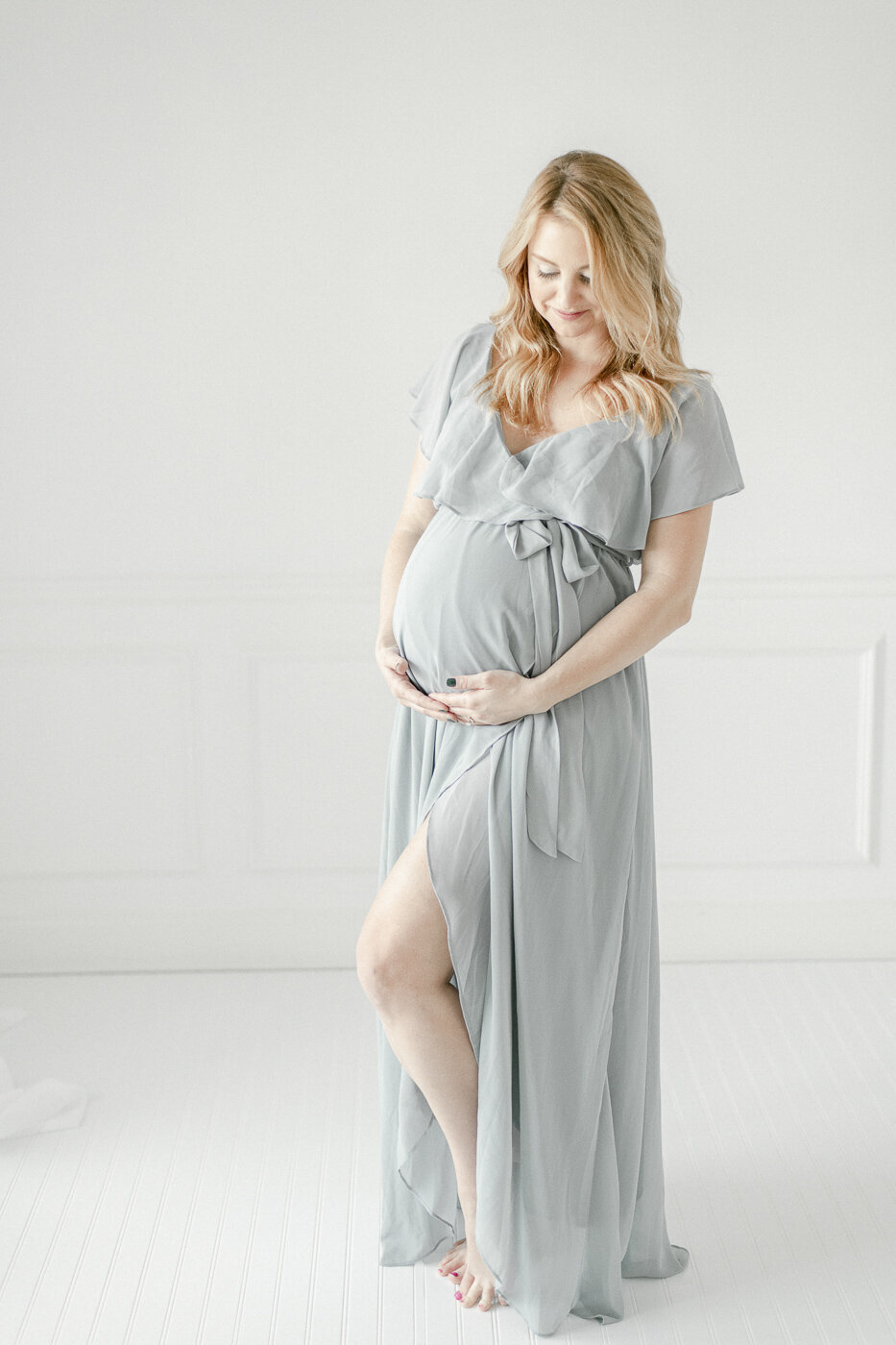 Pregnant woman in a blue maxi dress stands in a  white studio By Nashville maternity photographer Kristie Lloyd