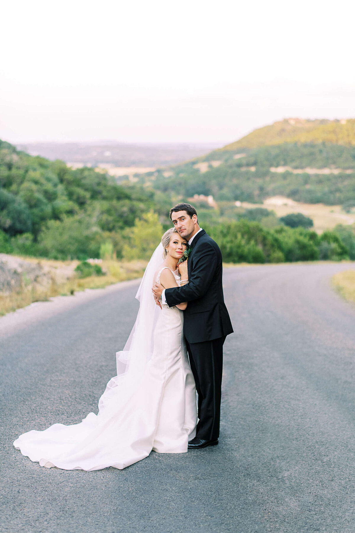 Bride and groom embrace overlooking Texas hill country landscape