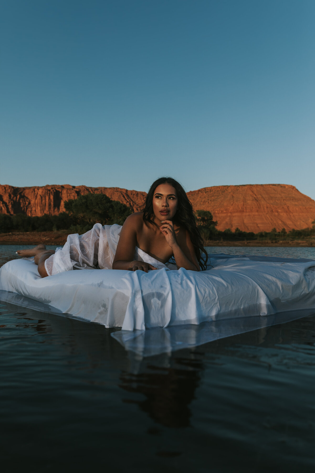 Woman is floating on a blow up mattress in the middle of the lake with only sheets covering her