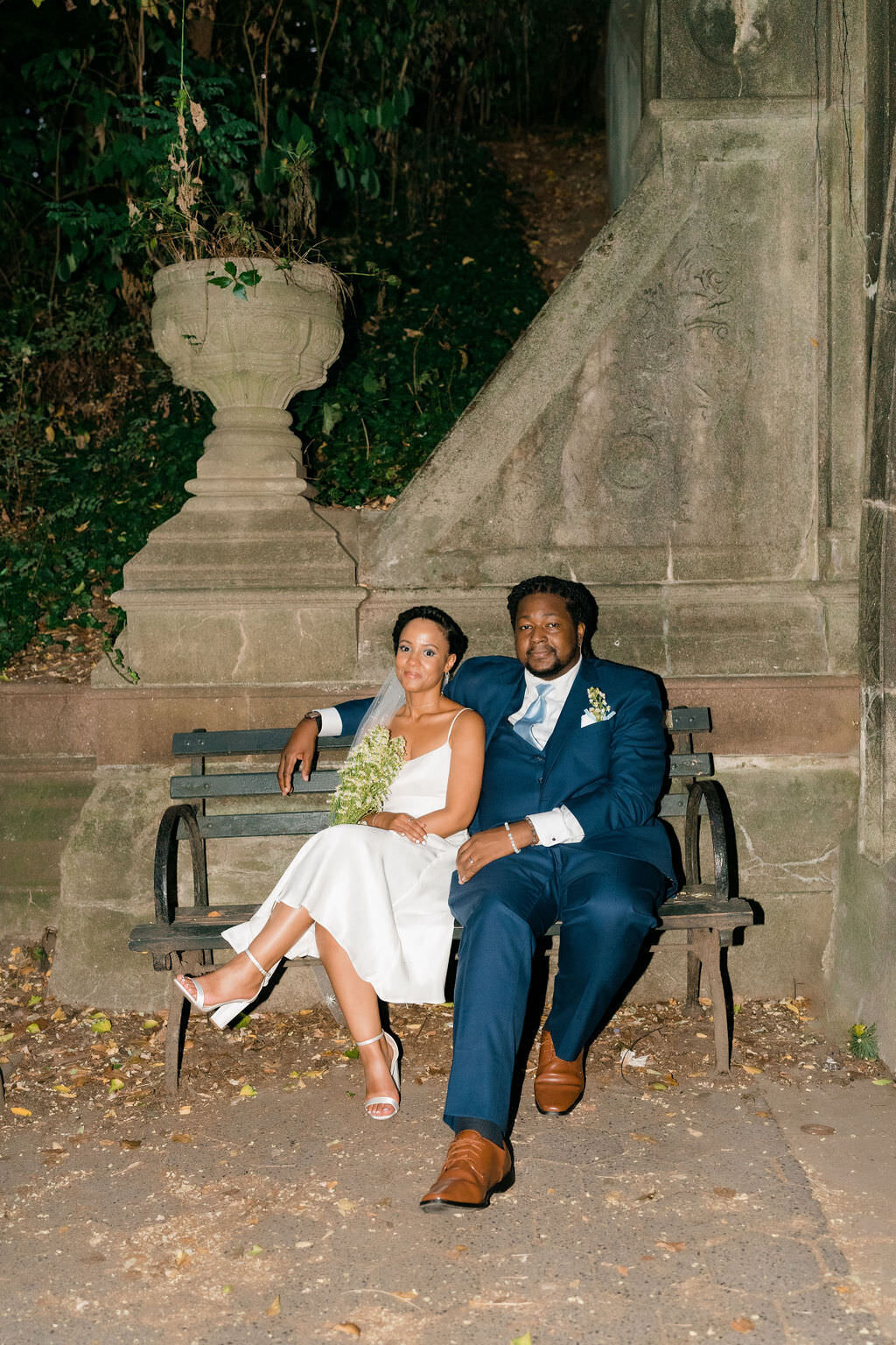 bride leaning up against groom as they sit on a park bench at night