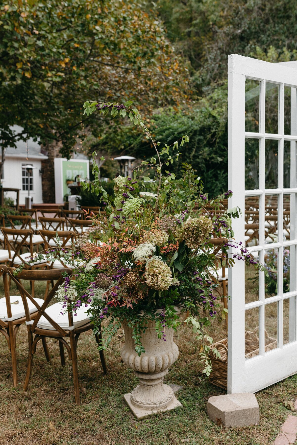 Lush ceremony urn arrangement overflowing with hydrangea, queen anne’s lace, greenery, and textural florals marking the entrance to an outdoor garden wedding aisle.