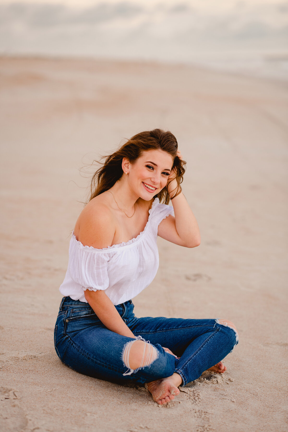 Girl on beach in white top and jeans for senior photography.