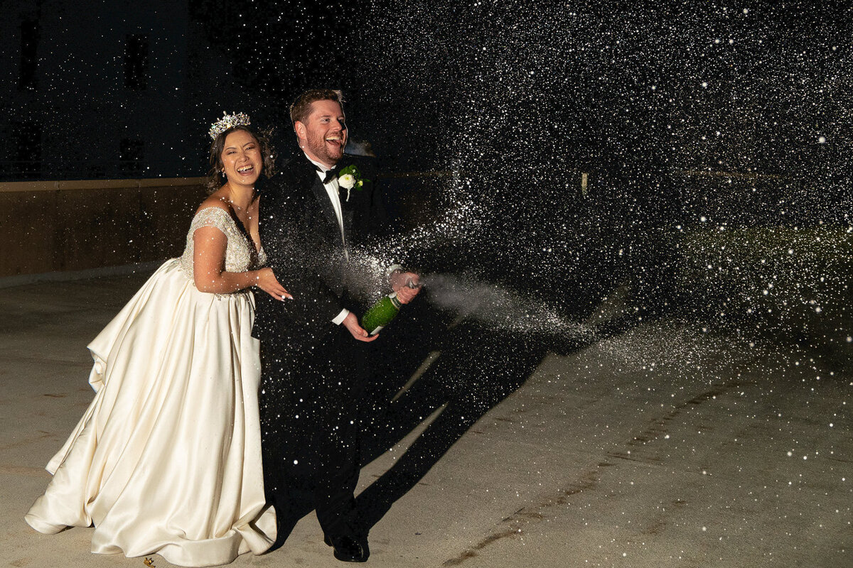Asian bride and groom spray champagne at night.