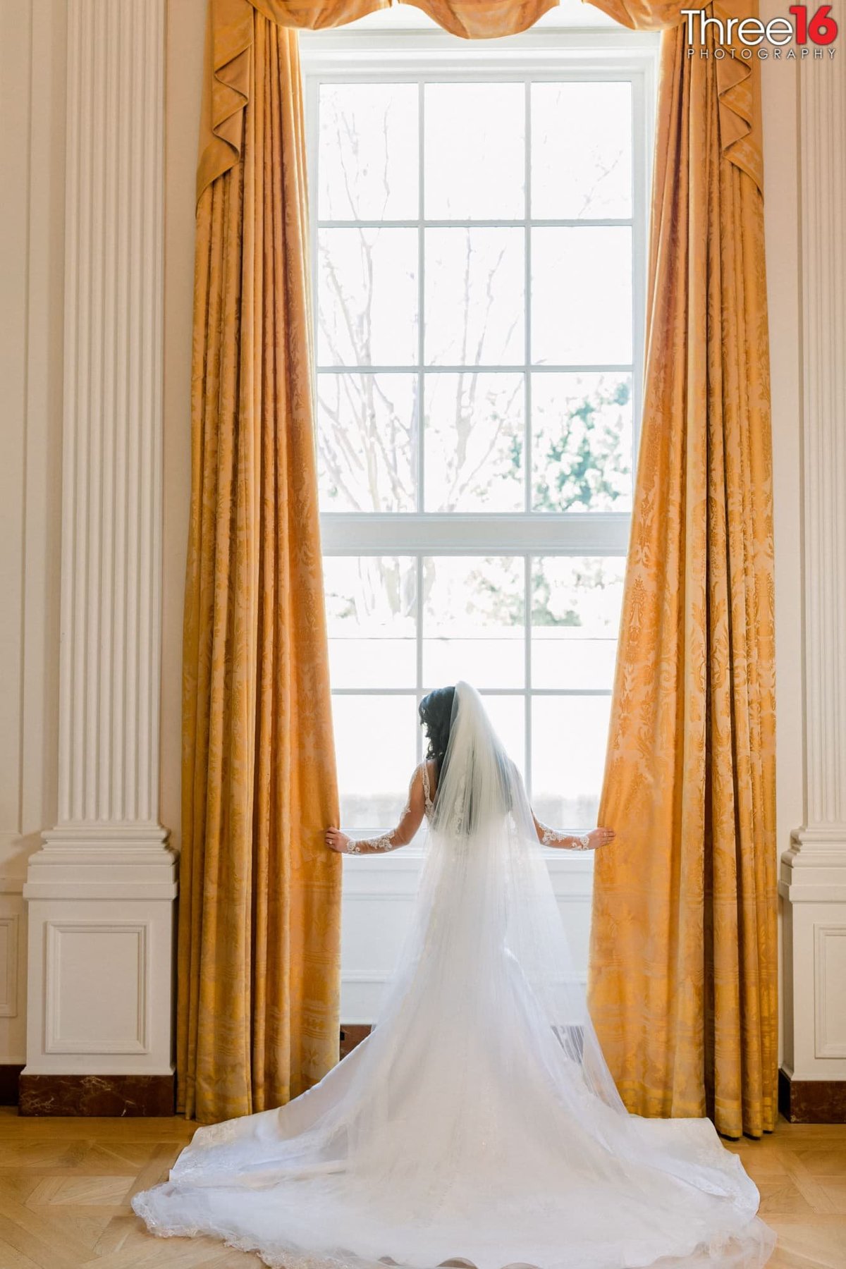 Bride poses in front of a large window with her gown train fanned out