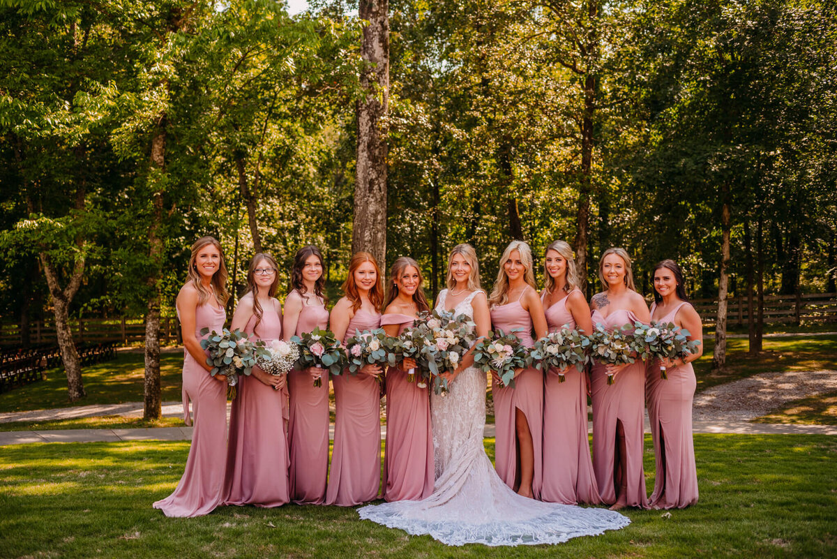Photo of bridesmaids wearing pink dresses standing next to the bride and smiling with bouquets in their hands