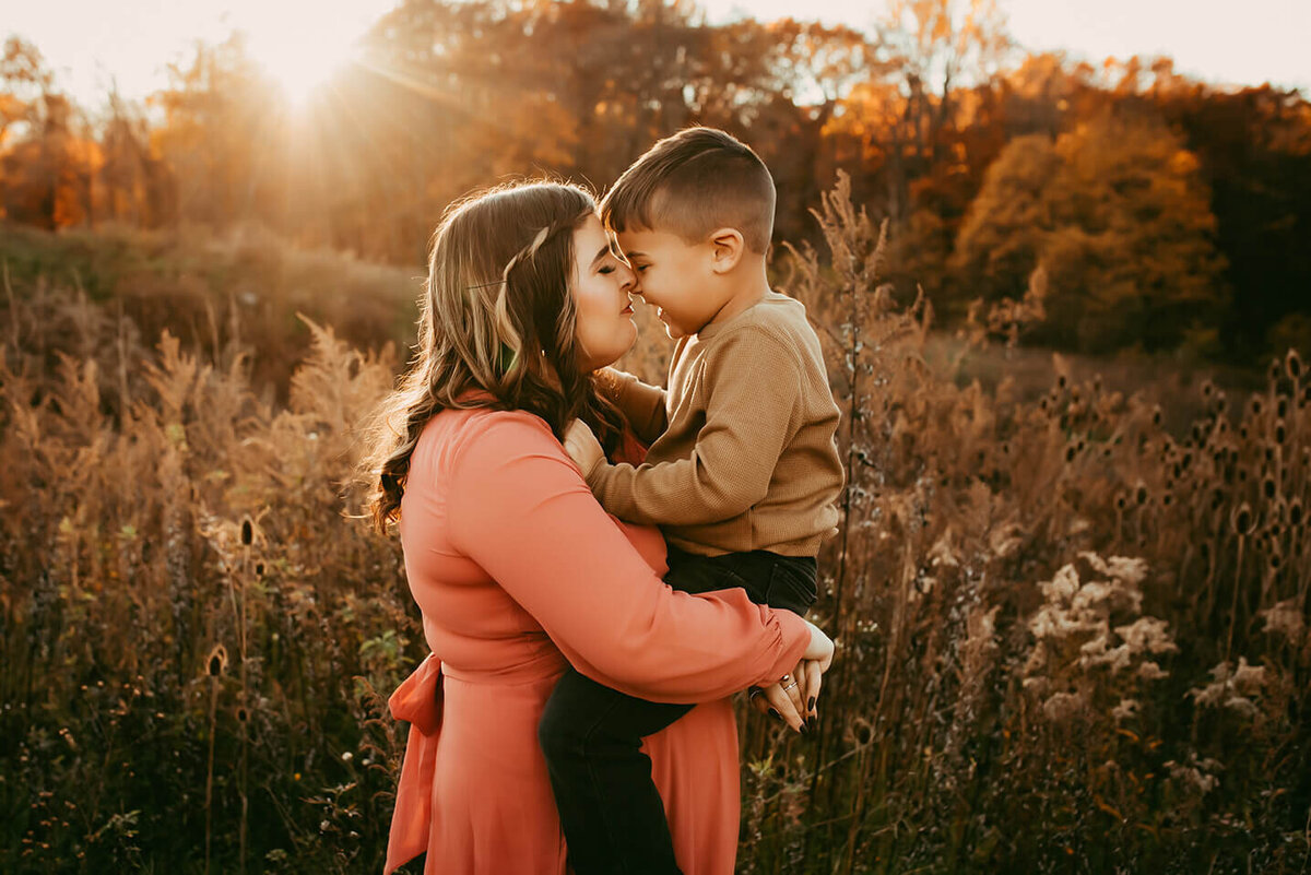 a mom holds her five year old son nose to nose in a field at sunset