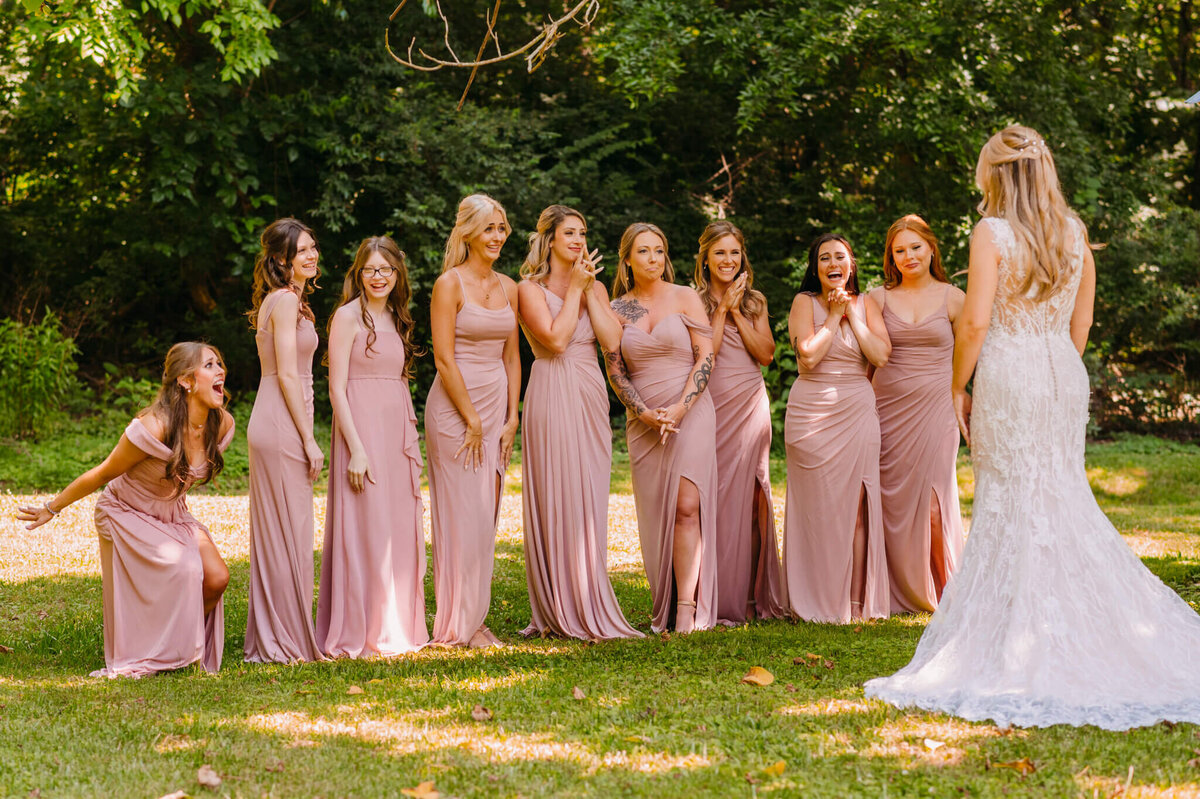 Photo of women wearing pink dresses and cheering as they see the bride for the first time