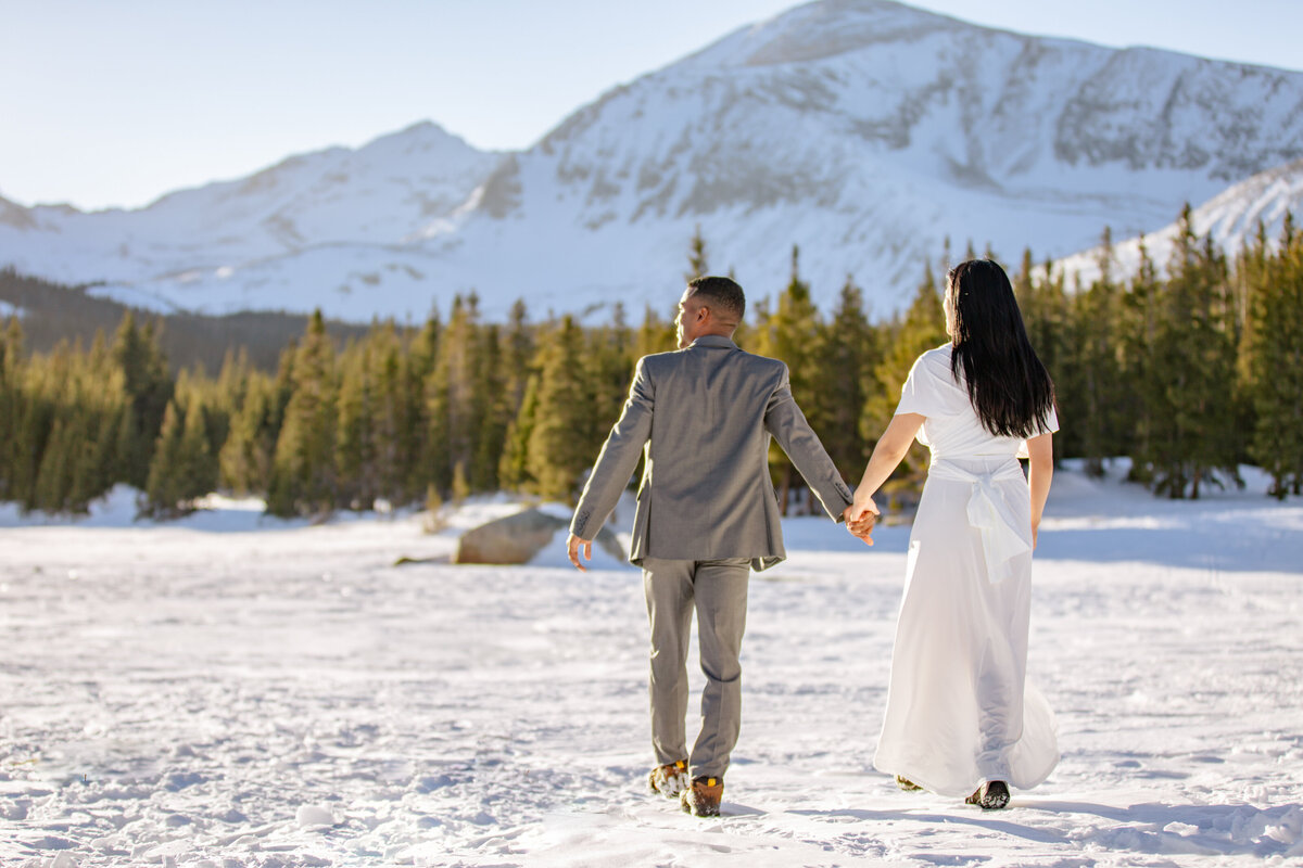 The bride and groom walk across a frozen lake enjoying the snowy mountain views