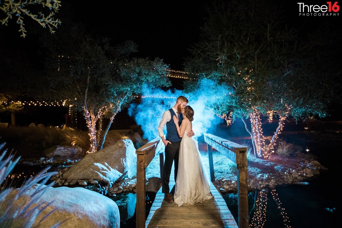Bride and Groom share a night time kiss on a bridge with a blue mist behind them