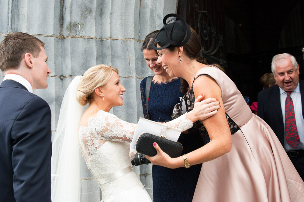 blonde bride wearing an a-line, lace, sleeved dress with satin waistband embracing her friends outside Killarney cathedral