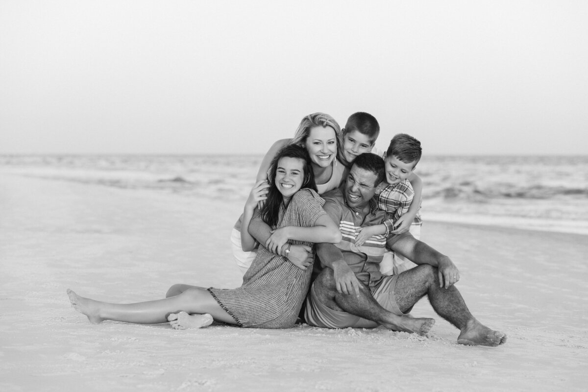 Black and white photo of a family sitting on the beach together smiling