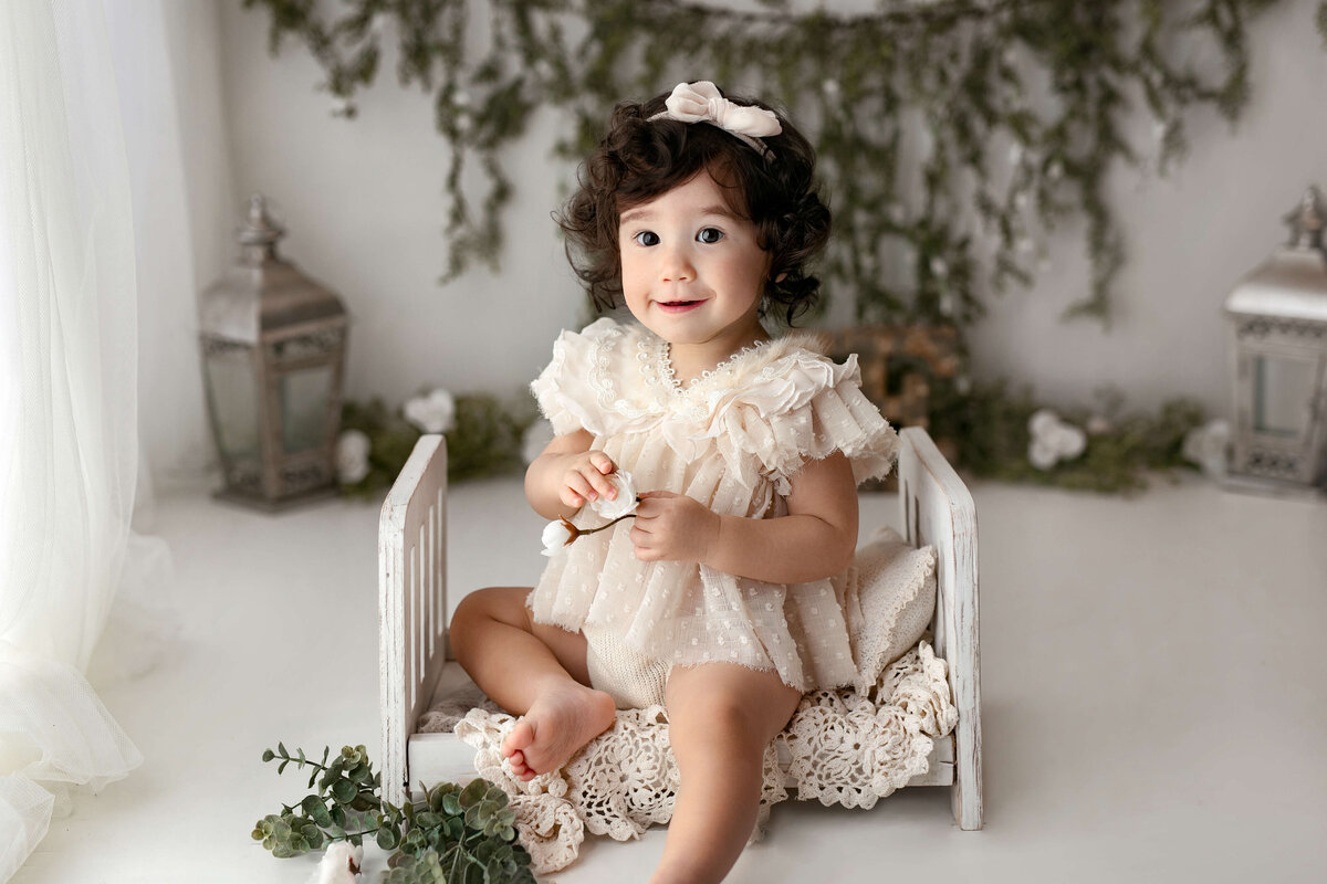 toddler sitting  on a bed wearing a       dress       at her milestone                    photography photo session