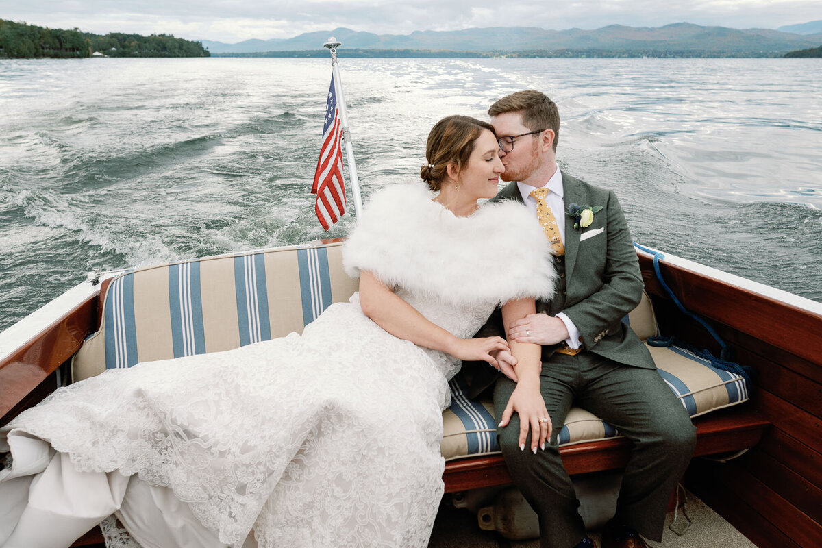 bride leans into groom on vintage criss craft boat at basin harbor club wedding in vermont