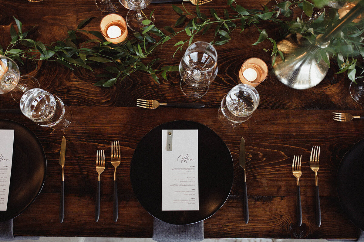 wedding reception table decor with black plates, candles and greenery
