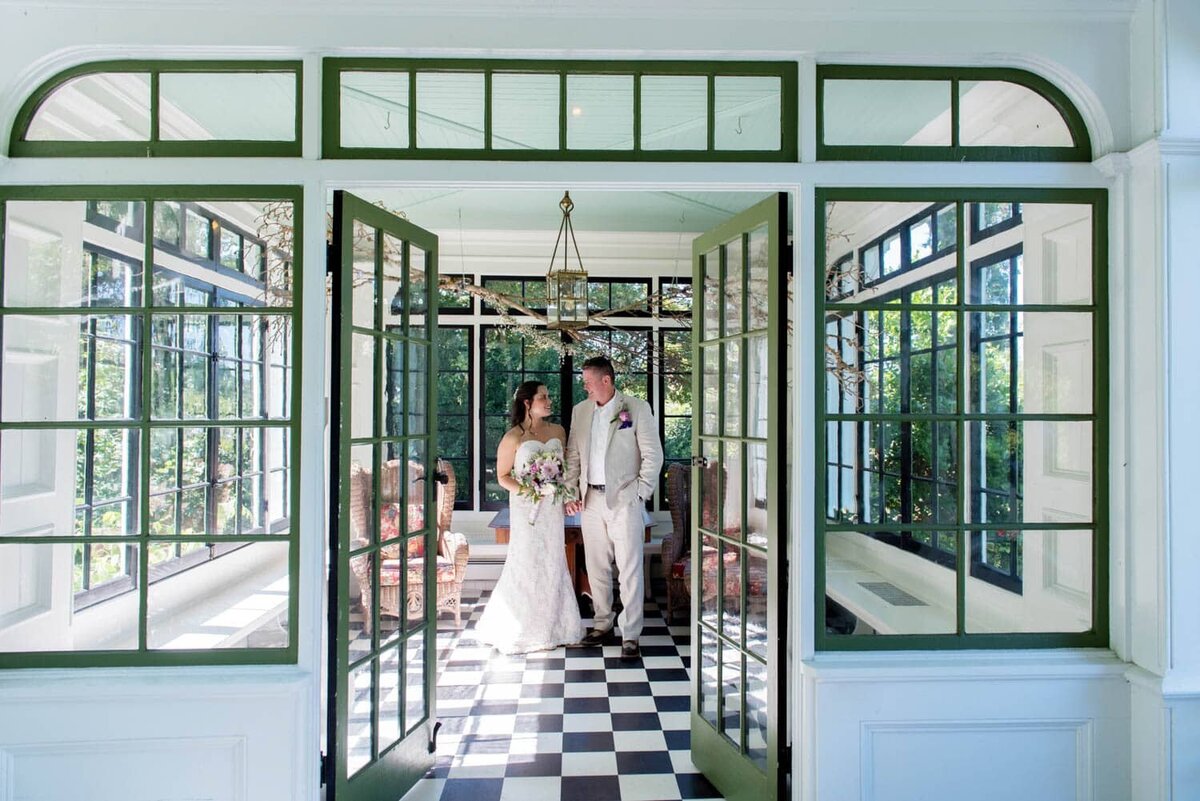 a bride and groom stand in the sun room at deepwood museum