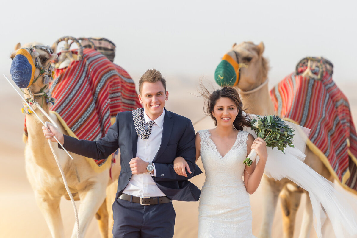 Portrait of the bride and groom with two camels celebrating their wedding in Dubai for a photoshoot organized by Lovely & Planned