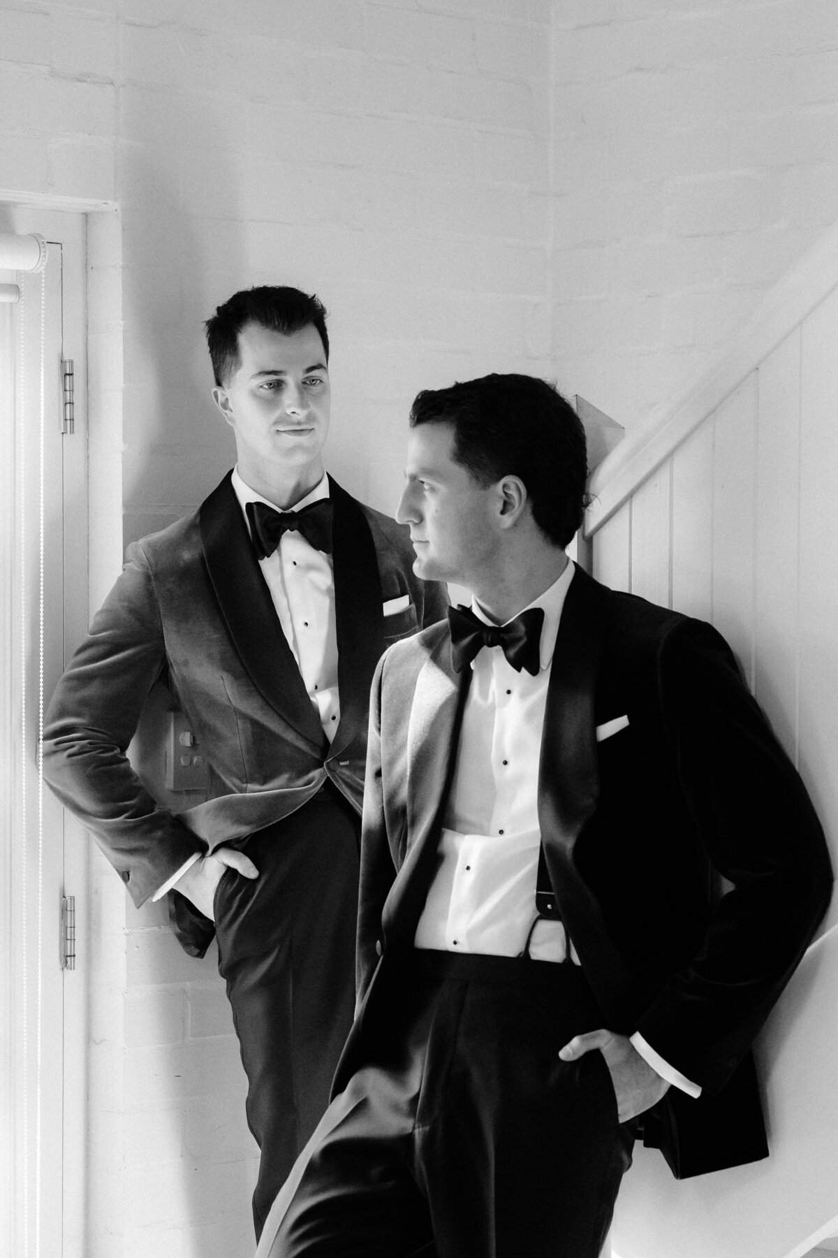 Black and white image of two grooms posing at the bottom of a staircase.