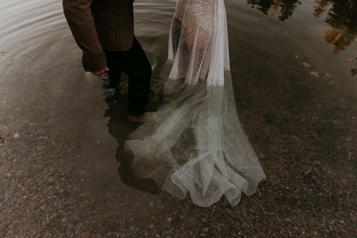 bride and groom legs as they walk into a pond in their wedding attire