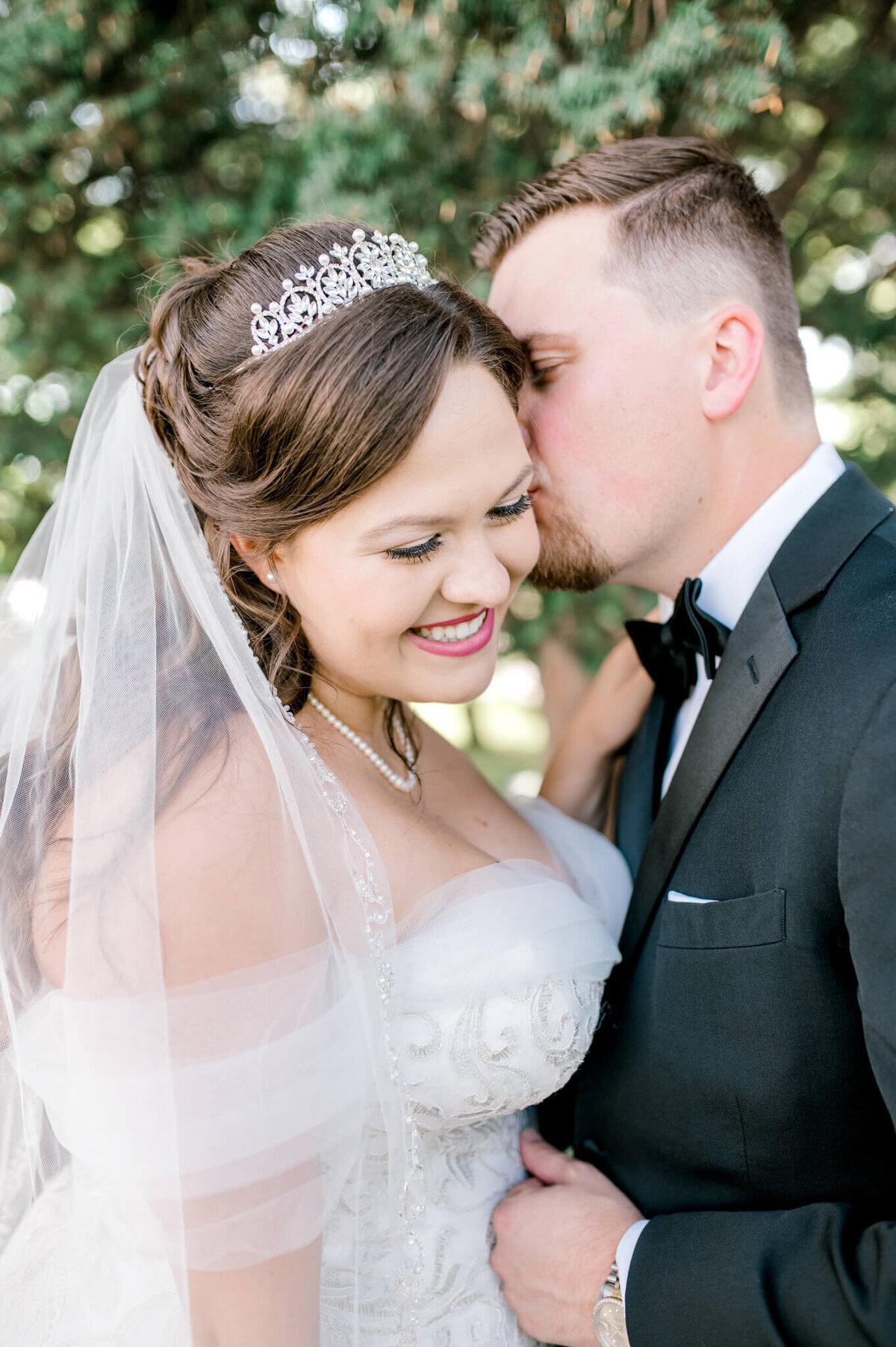 Groom kisses bride on the head and bride smiles with joy